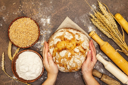 Preview: Female Hands Hold Freshly Baked Bread. Wheat Ears, Wooden Rolling Pins And A Bowls Of Flour And