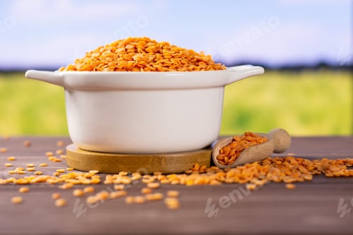 Preview: Lot Of Whole Raw Red Lentils In A Ceramic Stewpan With Green Wheat Field In Background