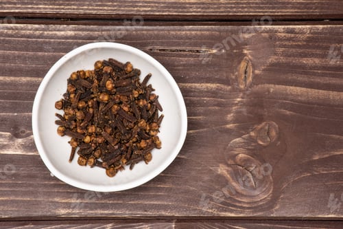 Preview: Lot Of Whole Small Dried Cloves Spice In A White Ceramic Bowl Flatlay On Brown Wood