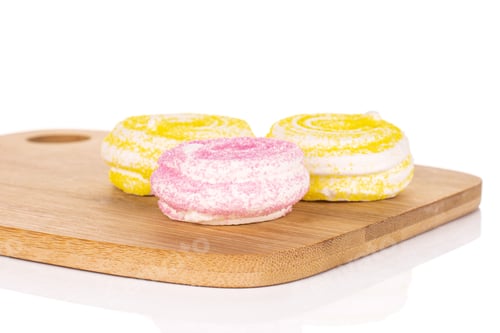 Preview: Group Of Three Whole Pink And Yellow Sweet Meringue On Bamboo Cutting Board Isolated On White