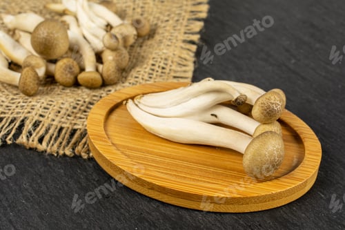 Preview: Lot Of Whole Fresh Brown Buna Shimeji Mushroom On Bamboo Coaster On Natural Sackcloth On Grey Stone