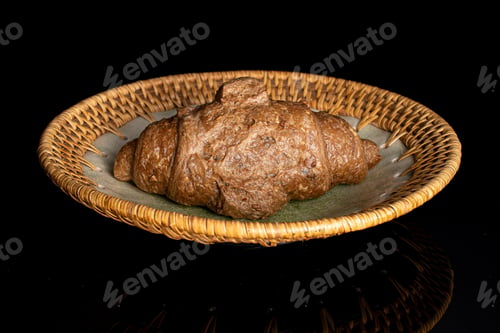Preview: One Whole Baked Wholegrain Croissant On Plate With Braided Edge Isolated On Black Glass