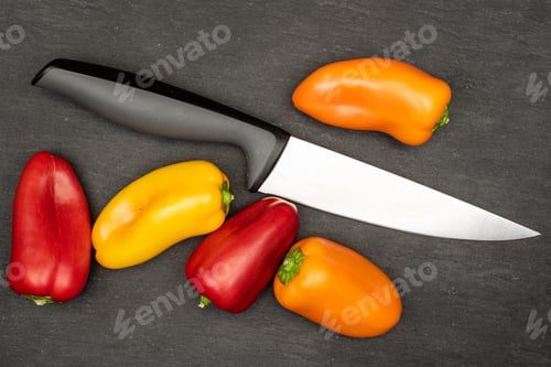 Preview: Group Of Five Whole Fresh Pepper With Steel Knife Flatlay On Grey Stone