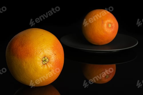 Preview: Group Of Two Whole Fresh Pink Grapefruit On Gray Ceramic Plate Isolated On Black Glass