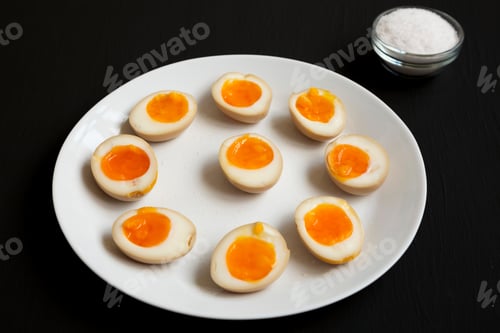 Preview: Homemade Unami Soy Sauce Eggs On A White Plate On A Black Background, Side View.