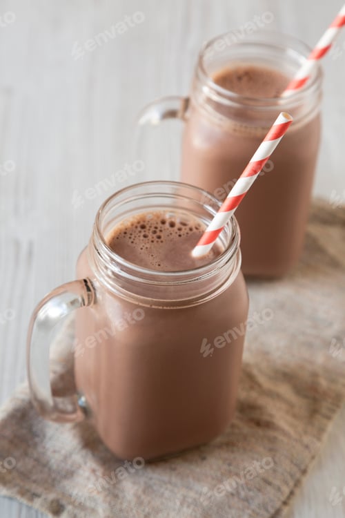Preview: Homemade New England Chocolate Milkshake In Glass Jar Mugs On A White Wooden Background, Side View