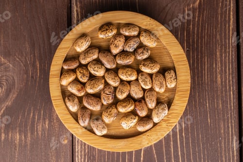 Preview: Lot Of Whole Mottled Brown Bean Pinto On Round Bamboo Coaster Flatlay On Brown Wood