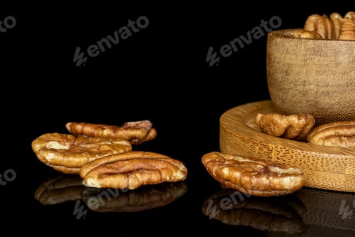 Preview: Lot Of Whole Tasty Brown Pecan Half On Round Bamboo Coaster In Glazed Bowl Isolated On Black Glass