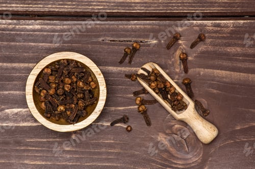 Preview: Lot Of Whole Small Dried Cloves Spice Scoop With Wooden Bowl Flatlay On Brown Wood