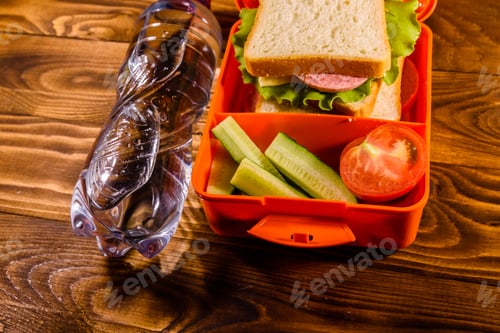 Preview: Bottle Of Water And Lunch Box With Sandwich, Cucumbers And Tomatoes On Rustic Wooden Table