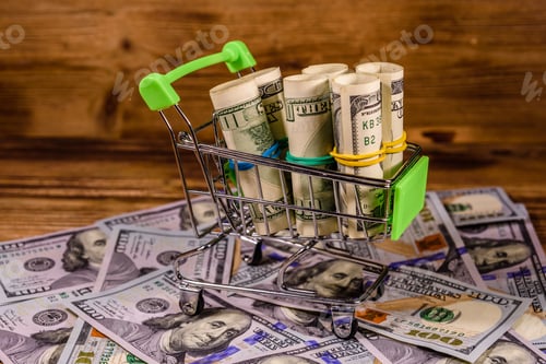 Preview: Small Shopping Cart With Rolled Up One Hundred Dollar Banknotes On Wooden Background