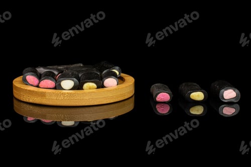 Preview: Lot Of Whole Sweet Black Liquorice Candy On Bamboo Coaster Isolated On Black Glass