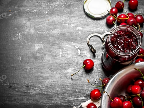 Preview: Cherry Jam And Metal Tool For Cherries. On A Black Wooden Background.
