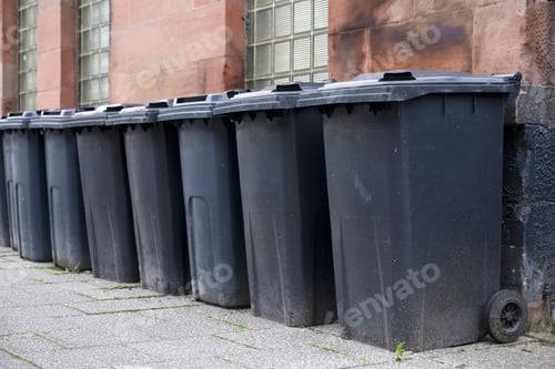 Preview: Black Wheelie Bins In A Row On Street With House Numbers Printed On Front Waiting For Bin Men To