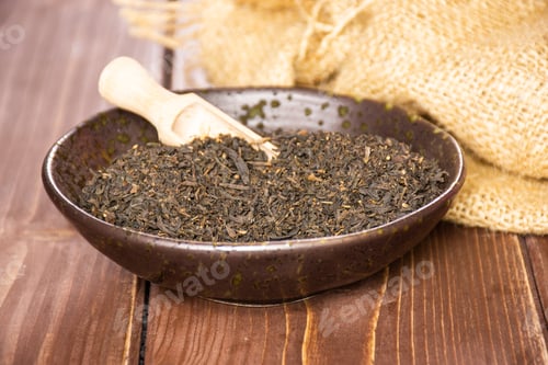 Preview: Lot Of Pieces Of Dry Black Tea Earl Grey In A Grey Ceramic Bowl With Wooden Scoop On Jute Cloth On