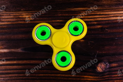Preview: Yellow Fidget Spinner On Rustic Wooden Desk. Top View
