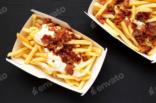 Preview: Top View, French Fries With Cheese Sauce And Bacon In Paper Boxes Over Black Background. Flat Lay