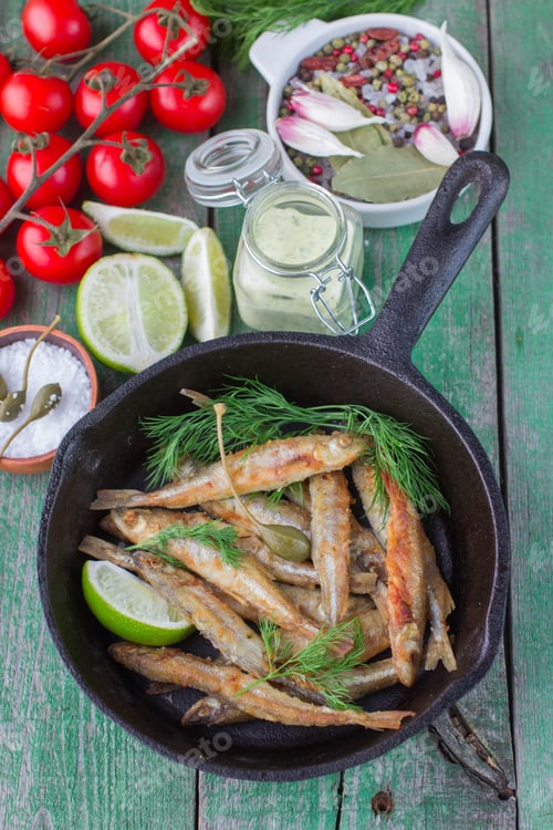 Preview: Fried Small Fish. Fried Smelt In The Pan On The Table With A Sauce, Lime, Tomatoes, Dill And Garlic