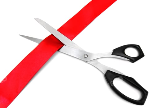 Scissors Cutting a Red Ribbon on White Backdrop
