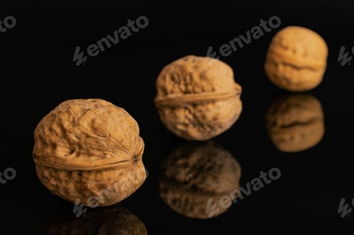 Preview: Group Of Three Whole Ripe Brown Walnut Placed Diagonally In Line Isolated On Black Glass