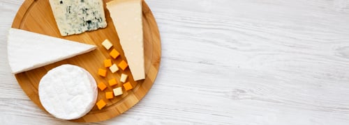 Preview: Tasting Cheese On Round Bamboo Board On A White Wooden Table. Food For Wine, Top View. Flat Lay