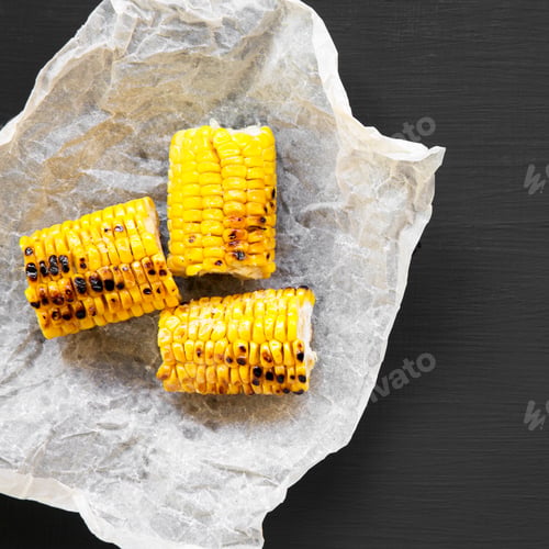 Preview: Grilled Corn On The Cob In Paper On Black Background, Overhead View. Summer Food. From Above, Flat