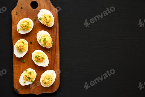Preview: Homemade Deviled Eggs With Chives On A Rustic Wooden Board On A Black Background, Top View. Flat