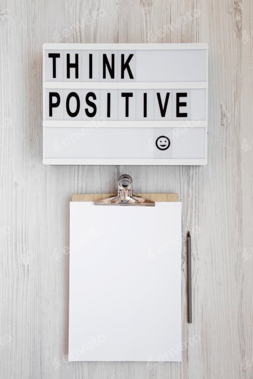 Preview: 'Think Positive' Words On A Modern Board, Clipboard With Blank Sheet Of Paper On A White Wooden
