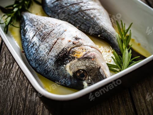 Preview: Fresh Dorada And Herbs In Cooking Pot On Wooden Background