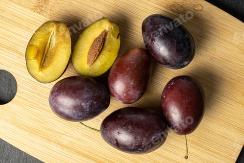 Preview: Group Of Five Whole Two Halves Of Sweet Purple Plum On Bamboo Cutting Board Flatlay On Grey Stone