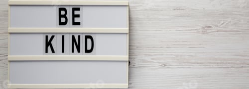 Preview: 'Be Kind' On A Lightbox On A White Wooden Background, Top View. Flat Lay, Overhead, From Above