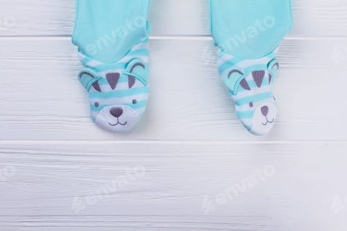 Preview: Footed Blue Baby Pajamas Legs. Close Up. Cartoon Bears, White Wooden Background.