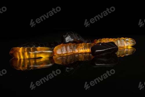 Preview: Group Of Three Whole Brown Orange Colourful Jelly Worm Candy Isolated On Black Glass