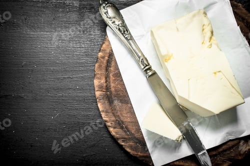 Vista previa: Mantequilla con un cuchillo en la tabla. En la pizarra negra
.