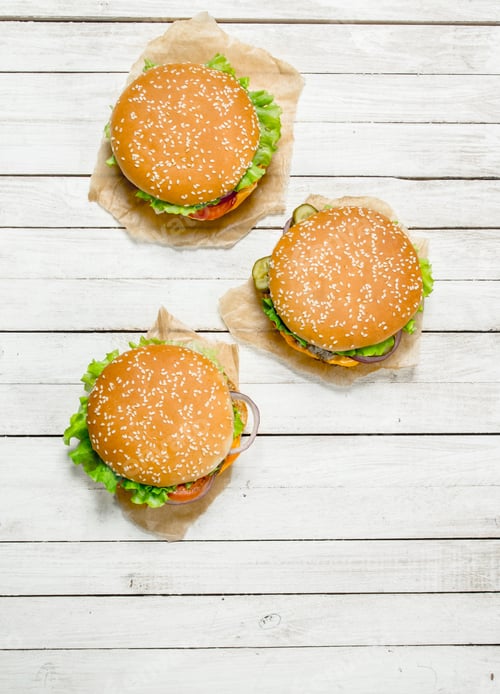 Preview: Burgers With Beef, Cheese And Vegetables On Paper. On A White Wooden Background.