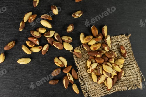 Preview: Lot Of Whole Raw Brown Brazil Nut On Natural Sackcloth Flatlay On Grey Stone
