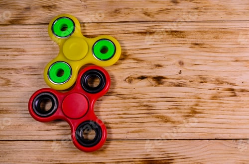 Preview: Yellow And Red Fidget Spinners On Rustic Wooden Desk. Top View