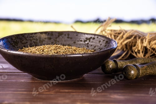 Preview: Lot Of Whole Roman Caraway Seeds In A Grey Ceramic Bowl With Green Wheat Field