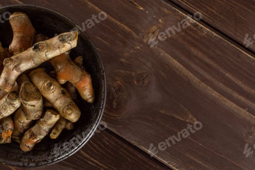 Preview: Lot Of Whole Bright Turmeric Rhizome Copyspace On Right On Grey Ceramic Plate Flatlay On Brown Wood
