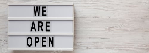 Preview: 'We Are Open' Text On A Lightbox On A White Wooden Surface, Top View. Flat Lay, Overhead, From
