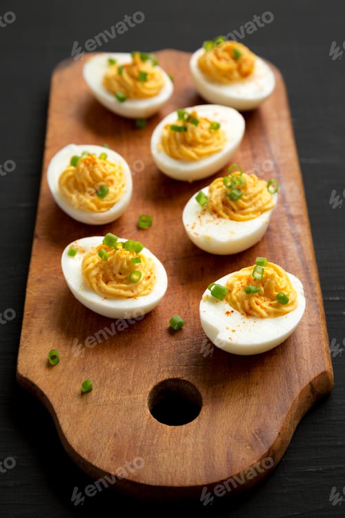 Preview: Homemade Deviled Eggs With Chives On A Rustic Wooden Board On A Black Background, Low Angle View
