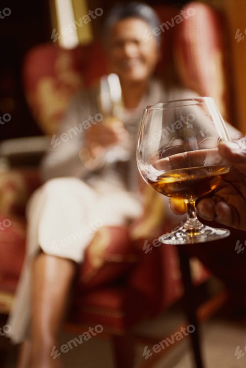 Preview: Man'S Hand Holding Snifter Of Brandy, Woman In Arm Chair In Background