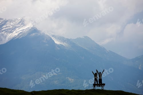 Preview: Young Couple Standing On Bench In Mountains Of Austria With Arms Outstretched