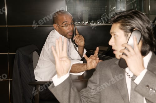 Preview: Two Businessmen Signaling To Each Other As They Talk On Different Telephones