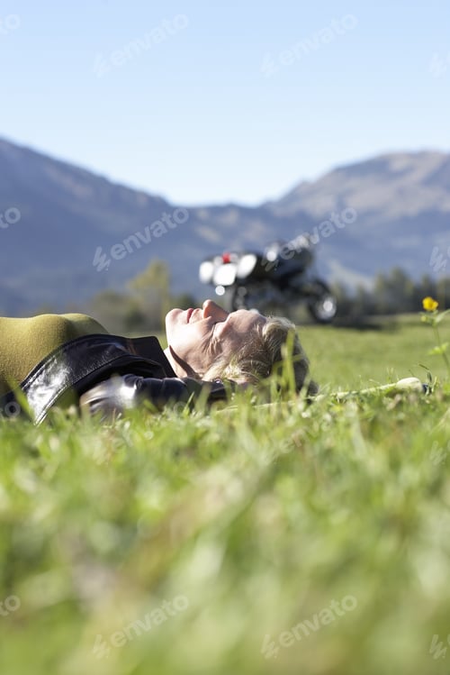 Preview: Woman Laying In Grass With Motorcycle And Mountains In Background