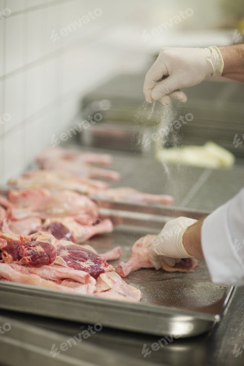 Preview: Close-Up Of Cook Wearing Rubber Gloves Seasoning Meat With Salt In Kitchen