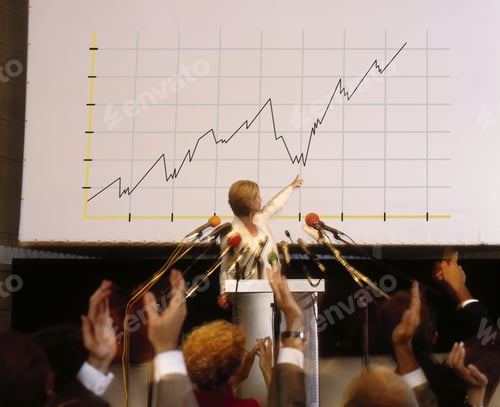 Preview: Businesswoman Speaking At Conference With Large Graph Chart