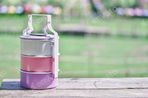 Preview: Tiffin Box Or Food Container Pastel Color On Wood Table And Green Nature Background, Used To Put