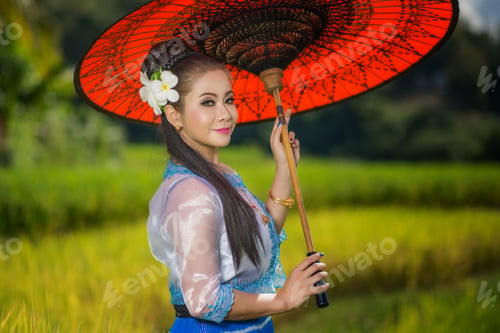 Preview: Beautiful Asian Girl In Myanmar Traditional Costume, With Red Bamboo Umbrella On On Rice Fields Sky