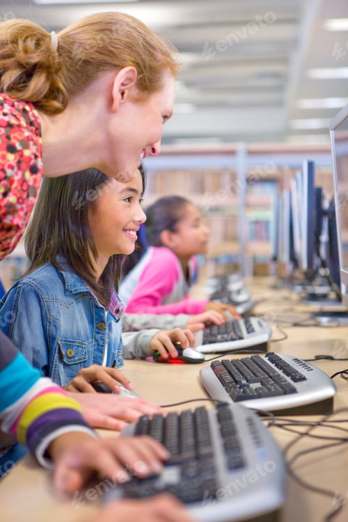Preview: A Portrait Shot Of A Teacher Helping A Young Girl In Using A Computer In A Computer Lab.